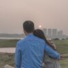 anonymous man embracing beloved while resting on lawn at sunset